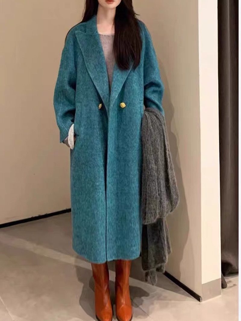 Woman wearing a long turquoise wool coat with gold buttons and brown boots.