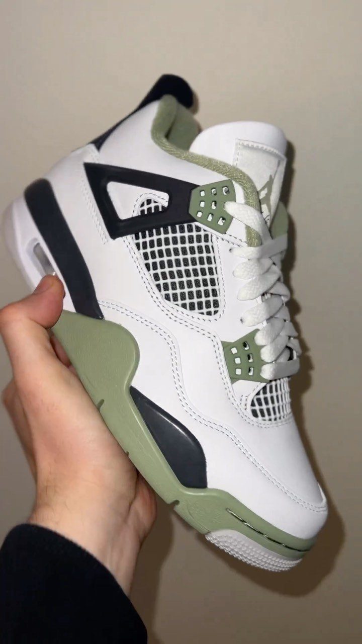 White Air Jordan 4 sneaker with seafoam green accents held by a hand.