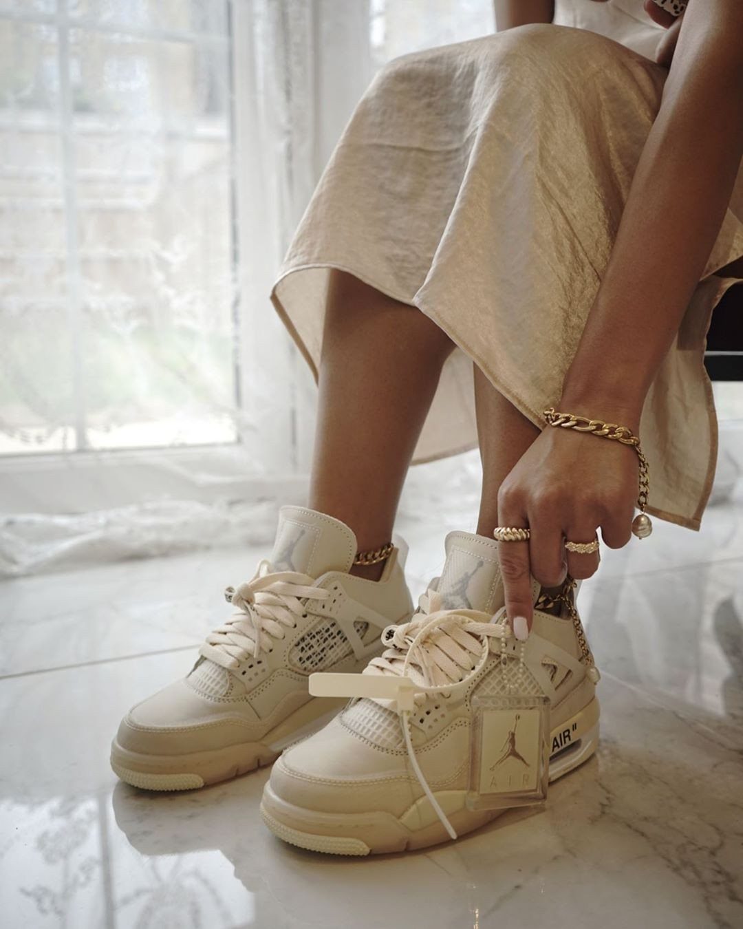 Cream Air Jordan sneakers worn by a person sitting on marble flooring.