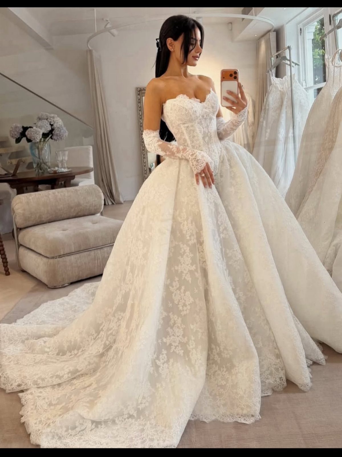 Woman in ivory lace strapless wedding gown with detached sleeves in a boutique.