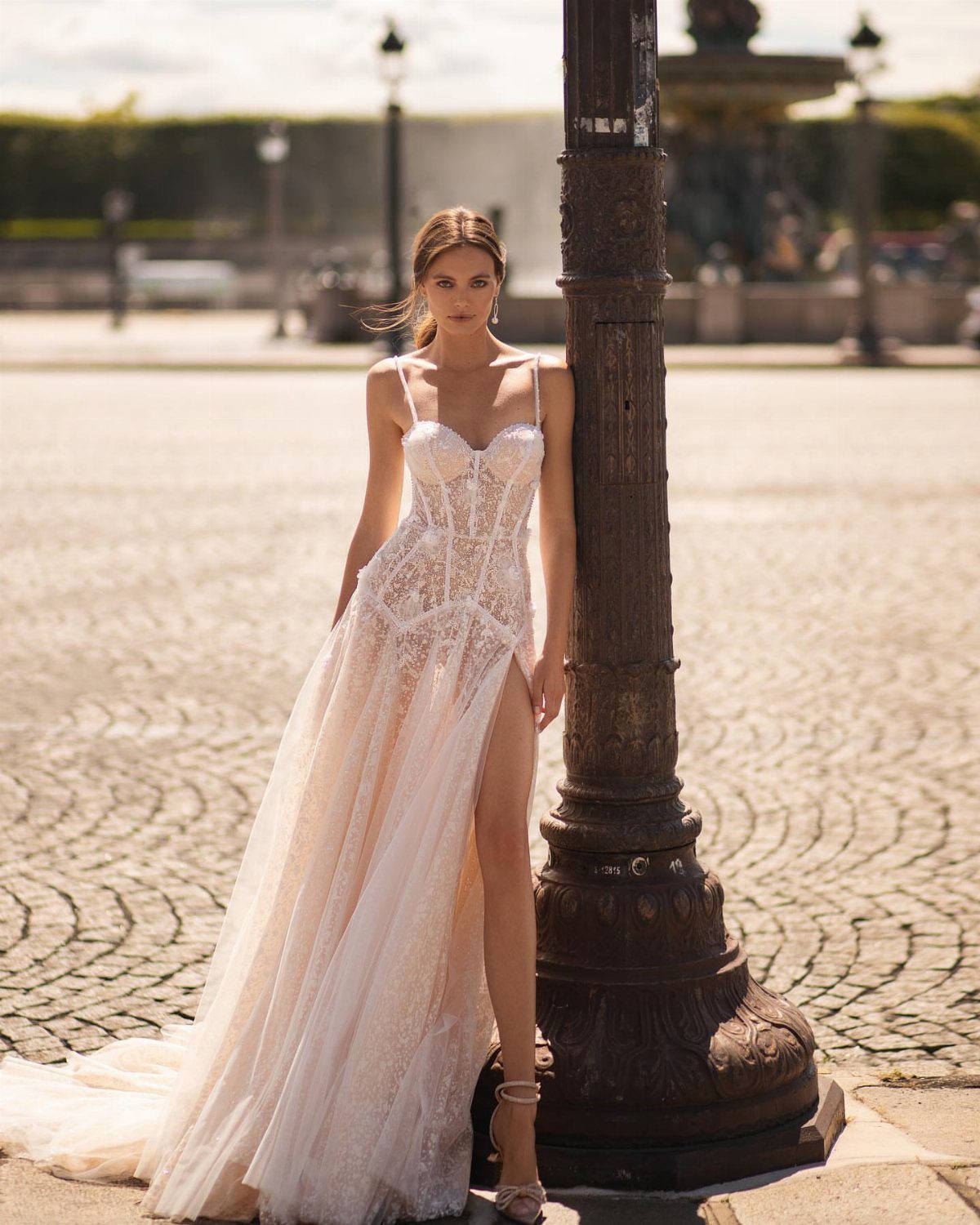 Woman in white floral lace wedding dress with high slit leaning on lamp post