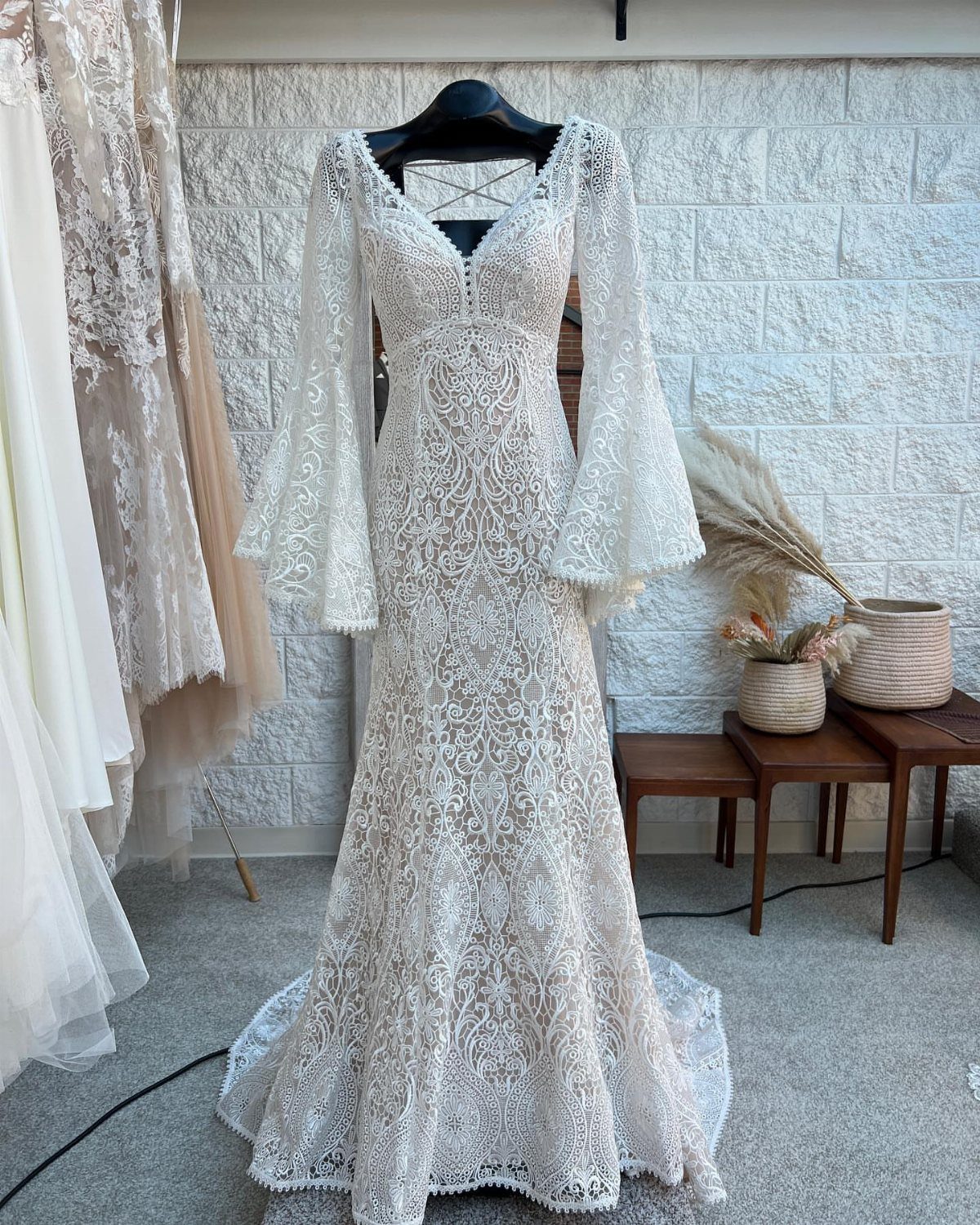 White floral lace wedding dress with long bell sleeves hanging against stone wall
