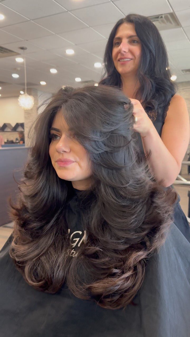 Woman with voluminous long dark brown hair and curtain bangs in a salon