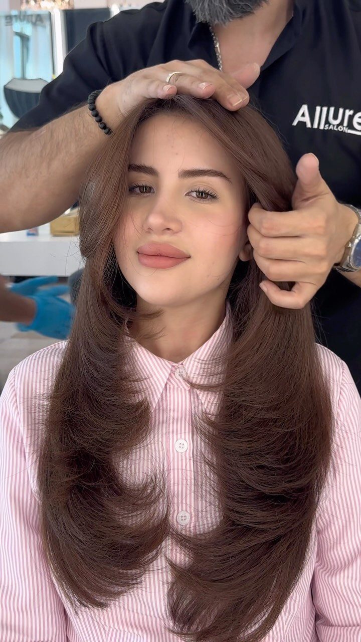 Woman with long brown hair featuring face-framing layers being styled by a professional.