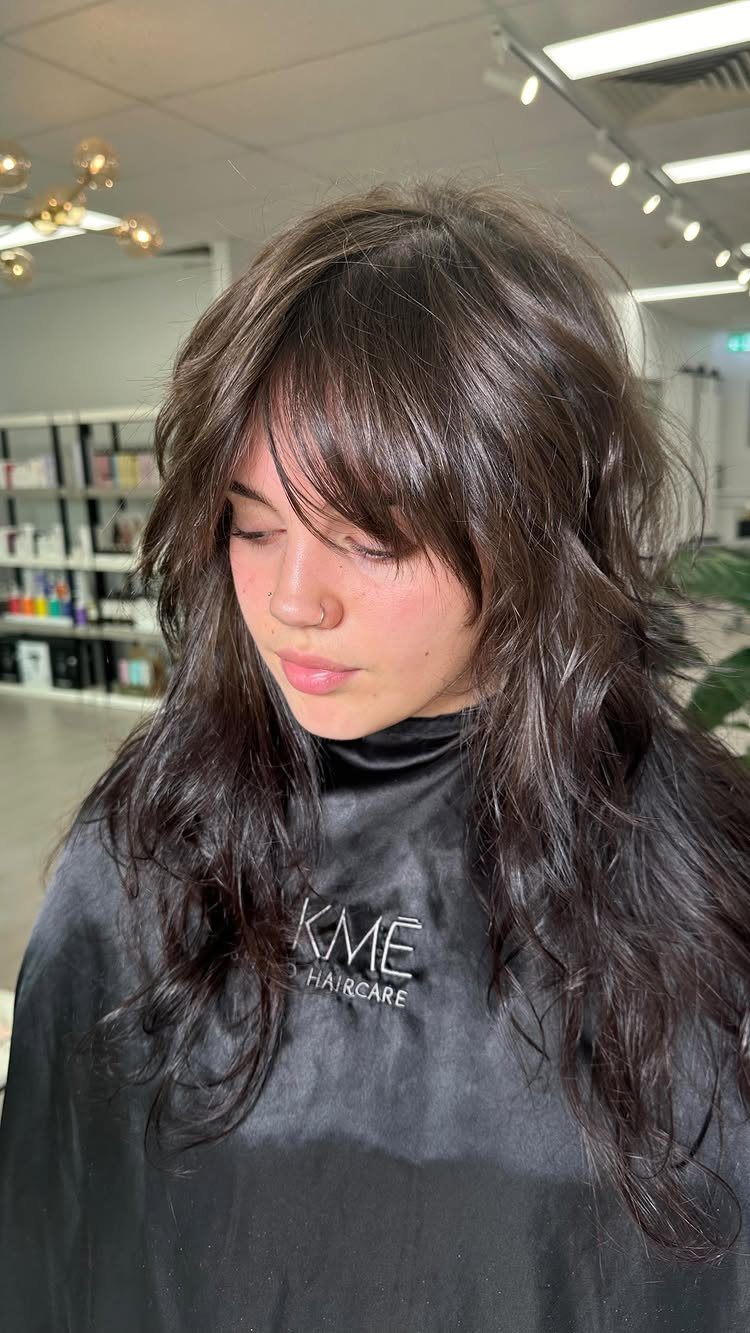 Woman with thick dark brown hair styled in heavy layers and bangs.