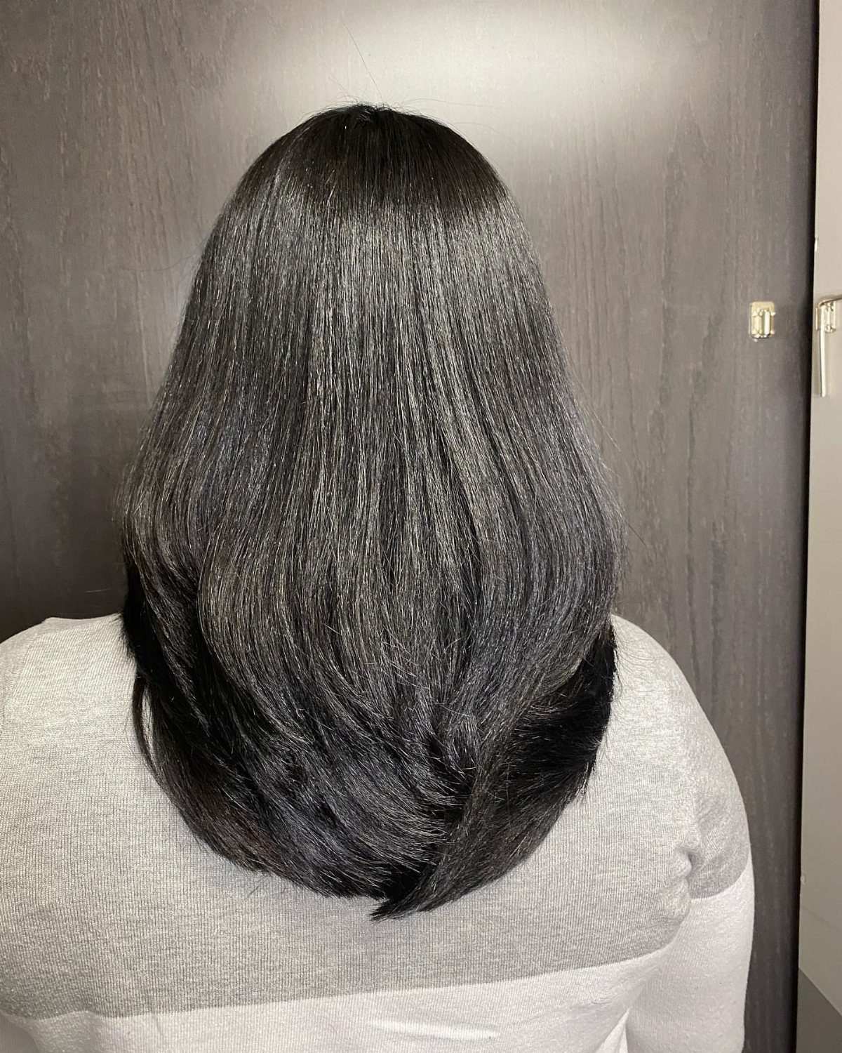 Thick black hair with visible layers curving inward, viewed from the back.