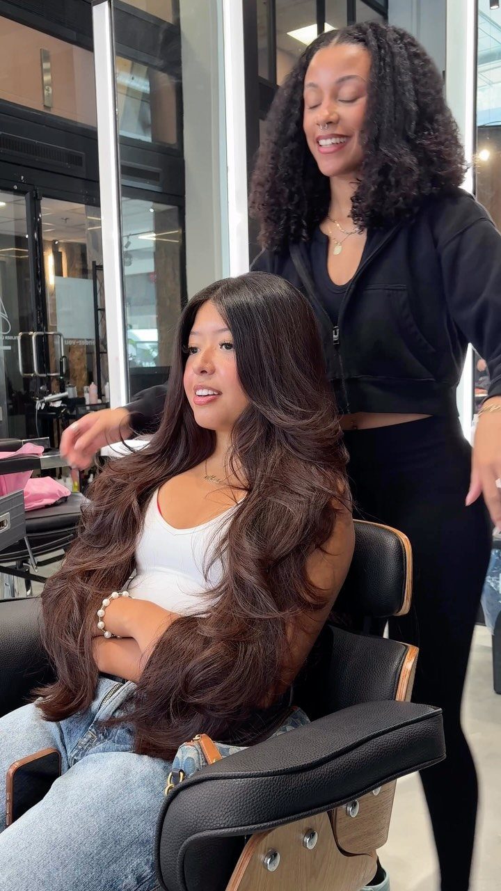 Woman with long brown butterfly cut hair sitting in a salon chair.
