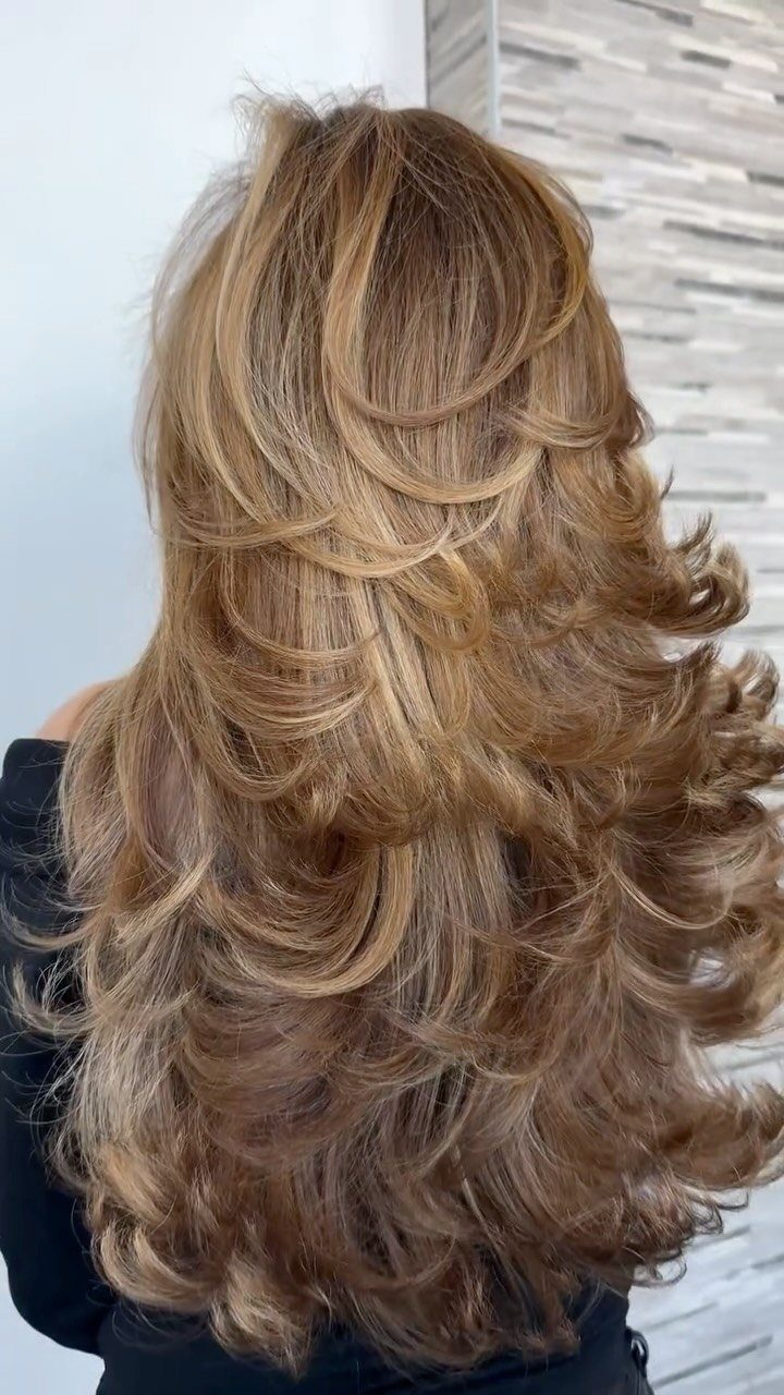 Long honey-blonde thick hair styled with voluminous cascading layers and curls from behind