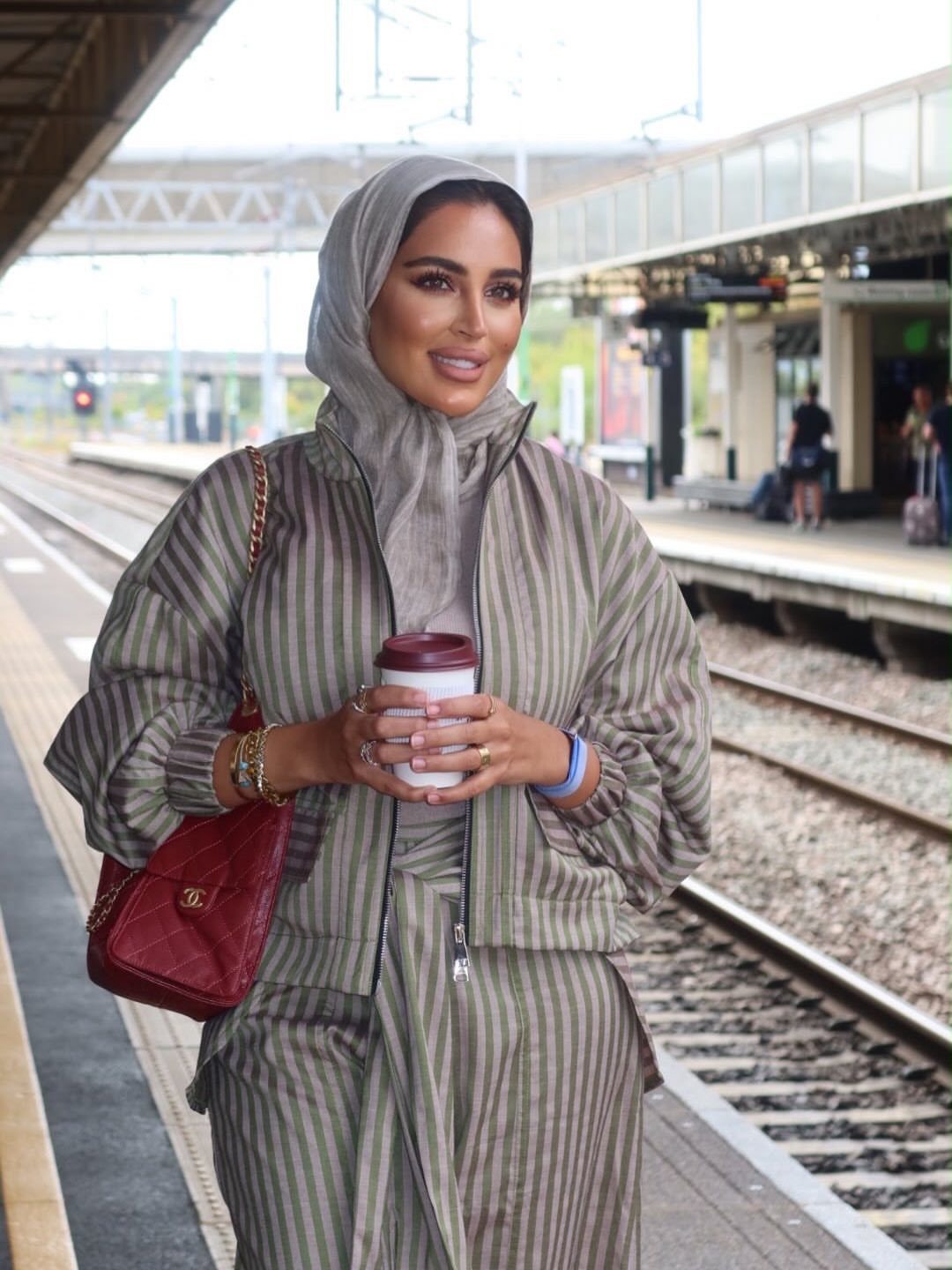 Woman in a grey hijab and striped coordinated set standing on a train platform.