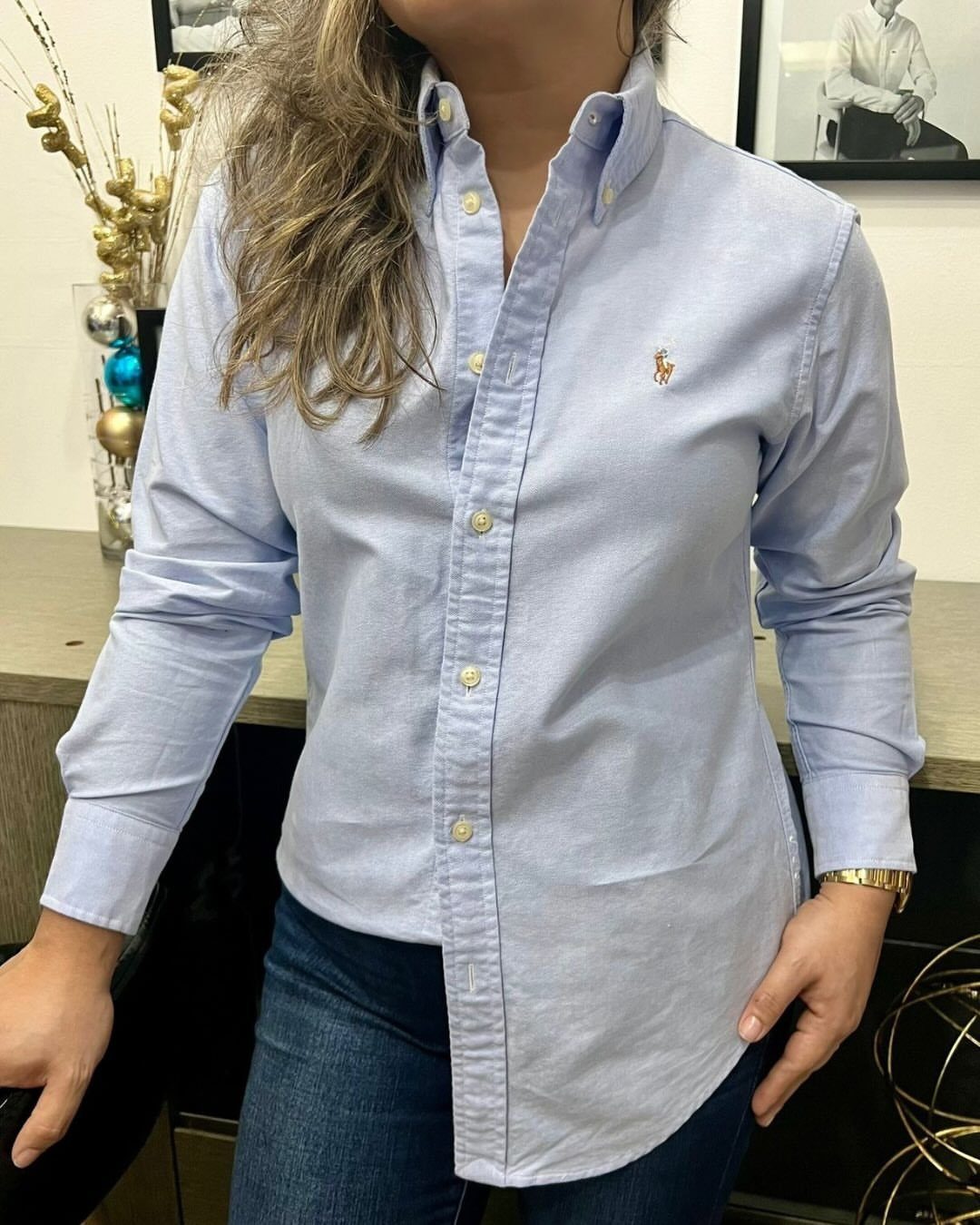 Person wearing a light blue Oxford shirt and dark blue denim jeans indoors.