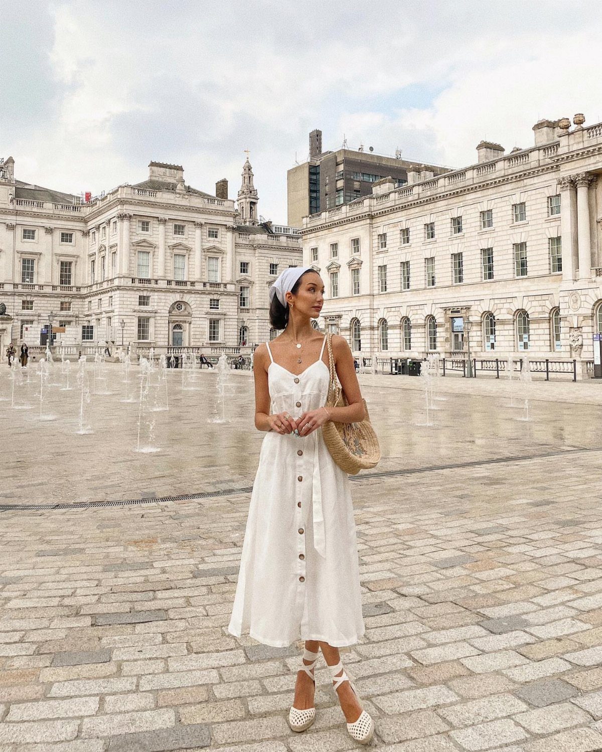 Woman in a white midi dress and headscarf carrying a straw basket bag.