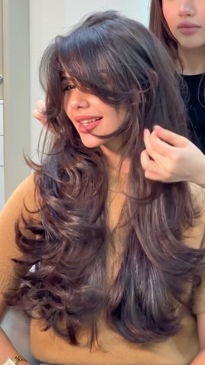 Woman with long brown layered hair and choppy bangs being styled by hands.