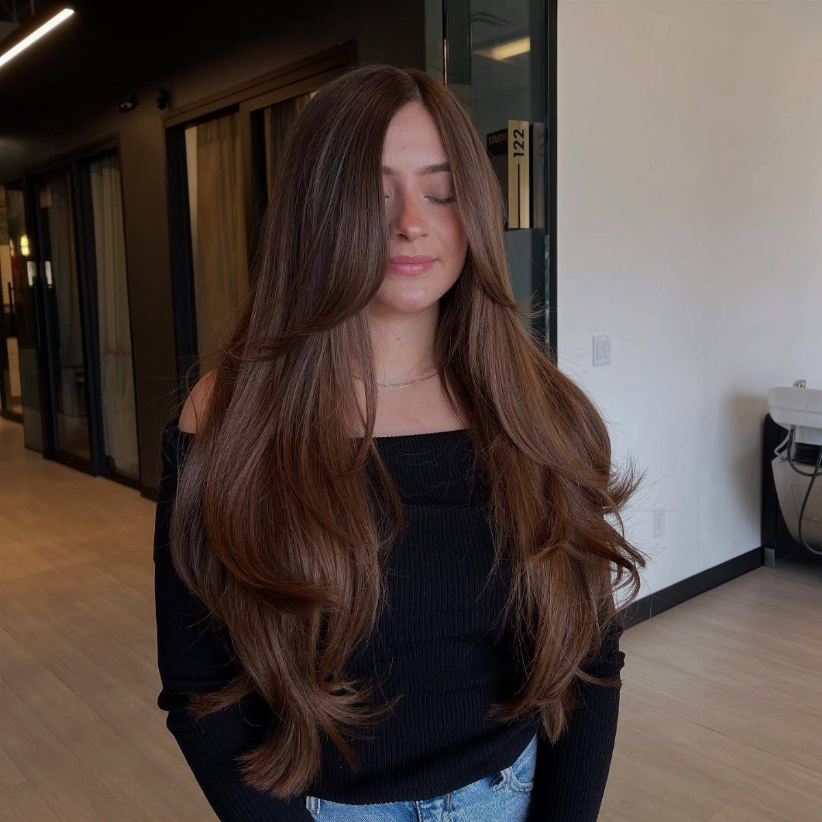 Woman with long reddish-brown hair featuring voluminous layers and face-framing highlights.
