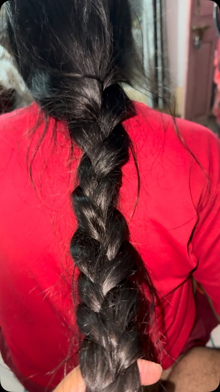 Long thick black hair styled into a chunky braid over a red shirt