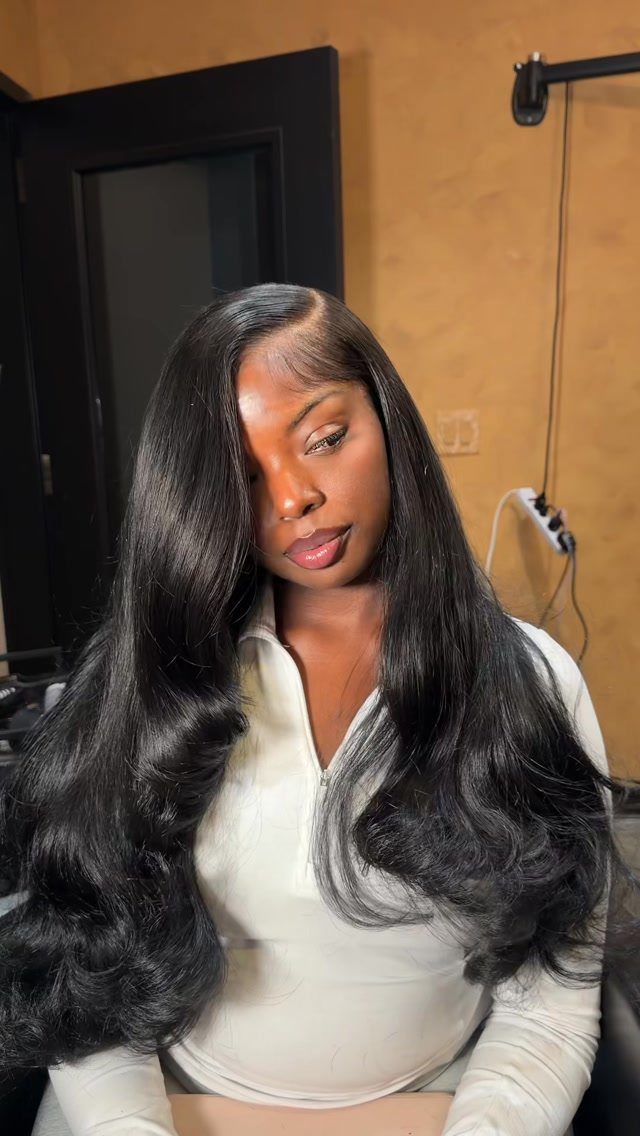 Woman with long thick wavy black hair styled in a deep side part