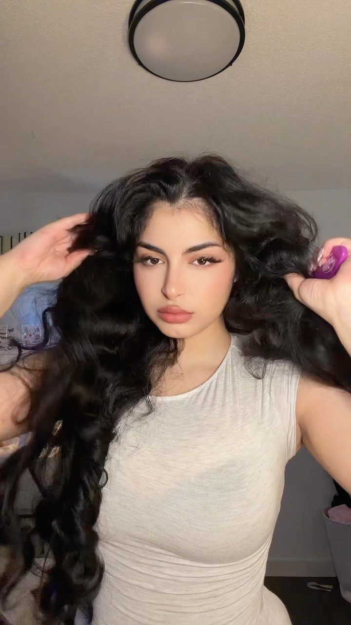 Woman with long, thick, dark curly hair posing in a white sleeveless top.