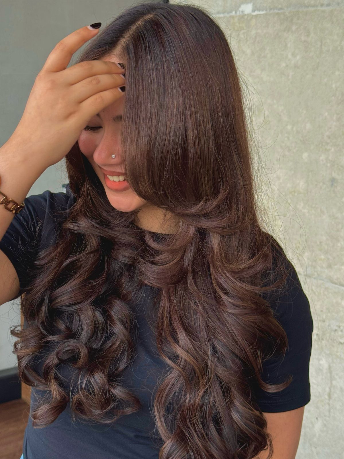 12 Long Brown Hair Ideas with Highlights, Curls and Layers 5 Woman with long wavy brunette hair and soft highlights posing against a wall