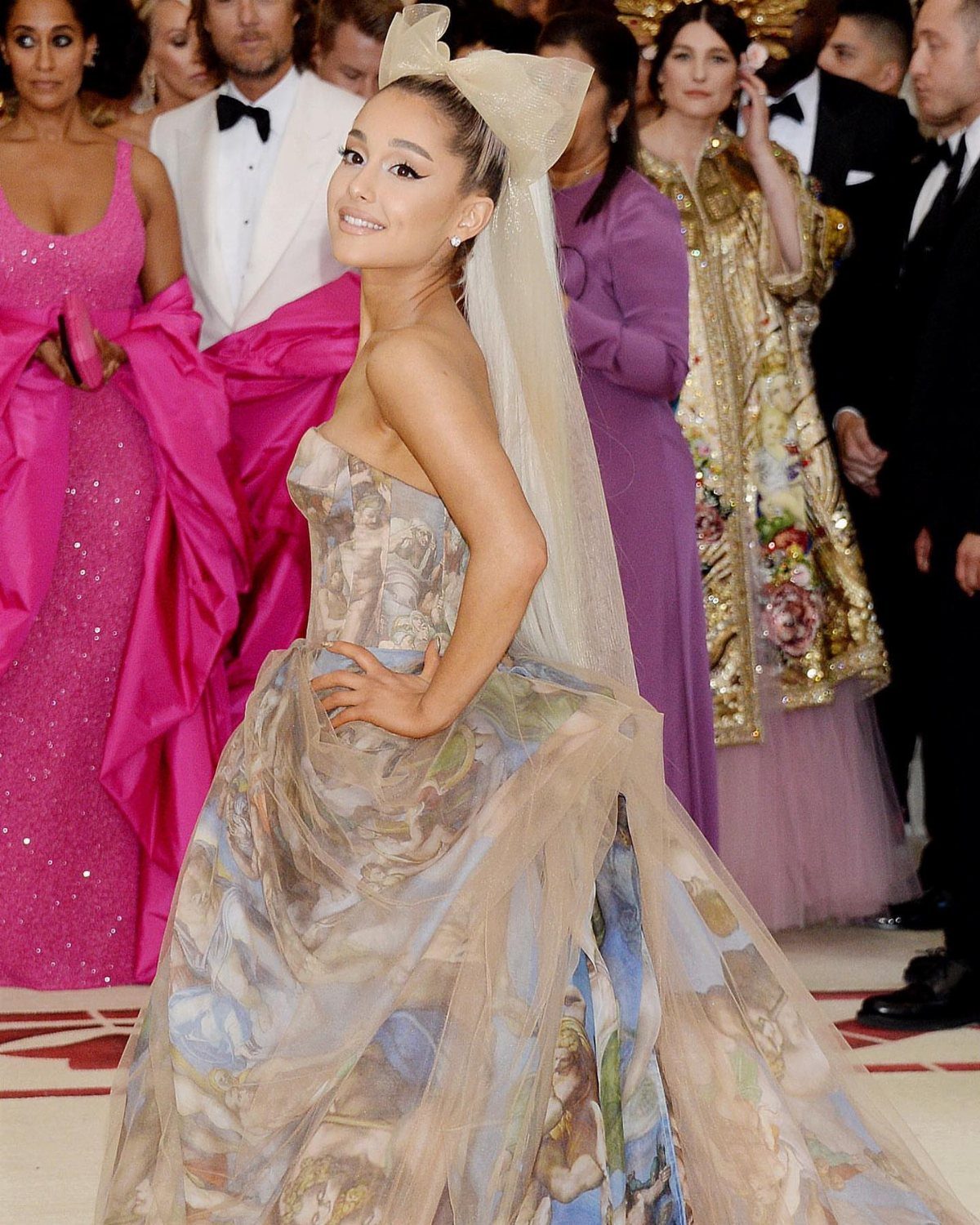 Ariana Grande in a classical art print gown and large bow headpiece.