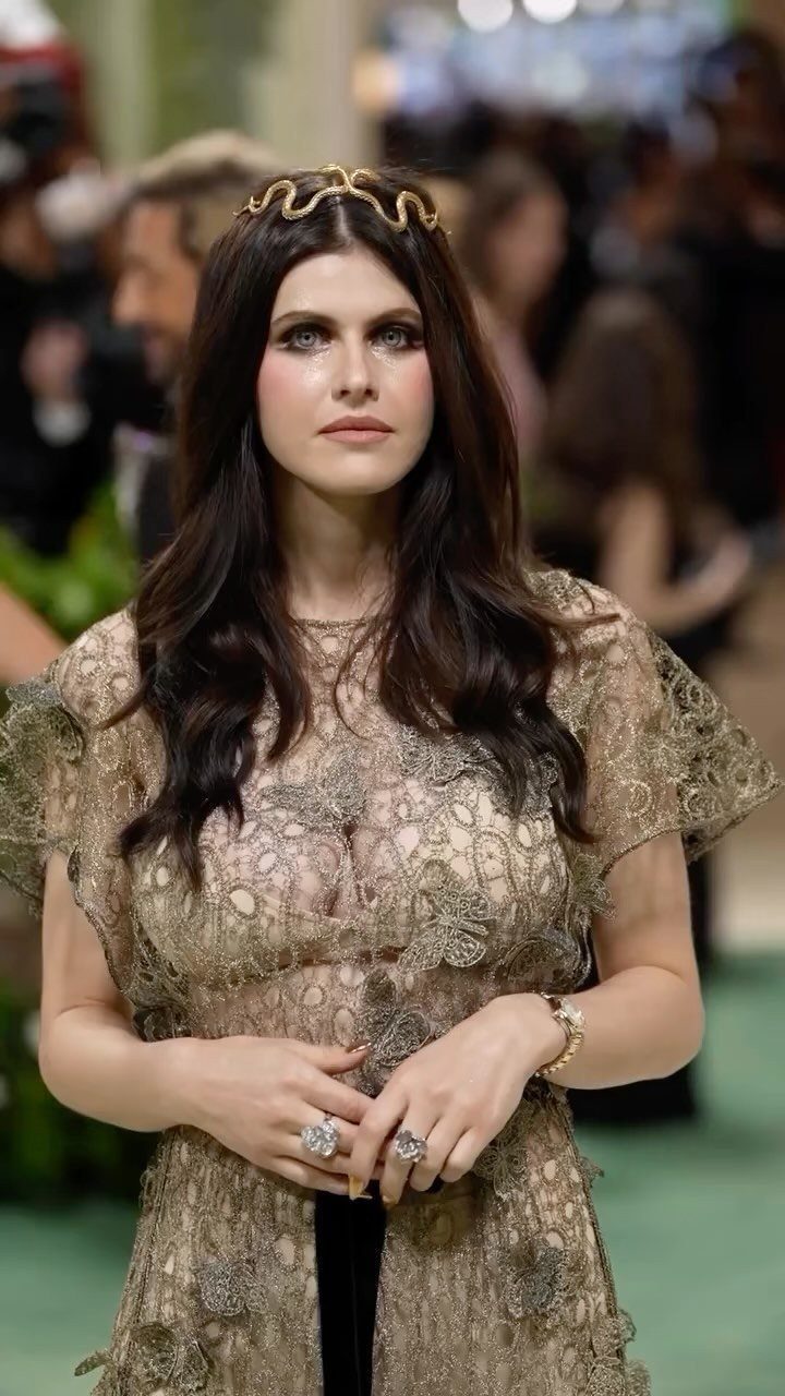 Woman in an ornate gold lace dress and snake crown on green carpet
