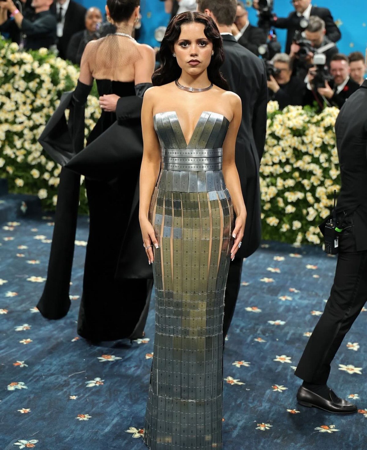 Woman in a strapless metallic silver mirrored gown posing on a blue carpet.