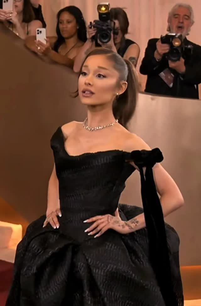 Ariana Grande in a structured black off-the-shoulder gown posing on a red carpet.