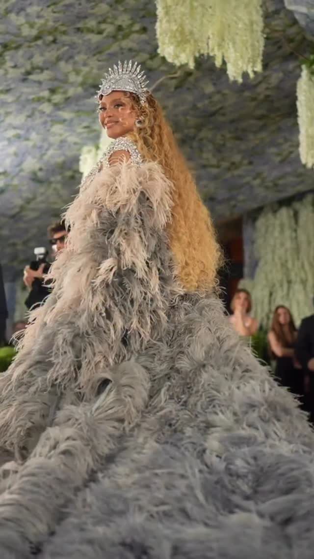 Woman in a voluminous grey feathered gown and silver crown posing at event