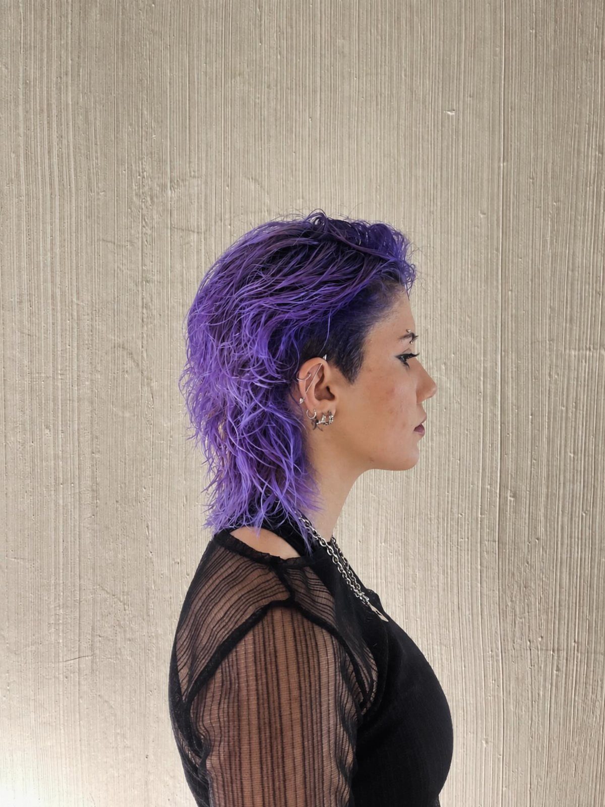 Person with purple wet-look mullet hair posing in profile against a neutral wall.