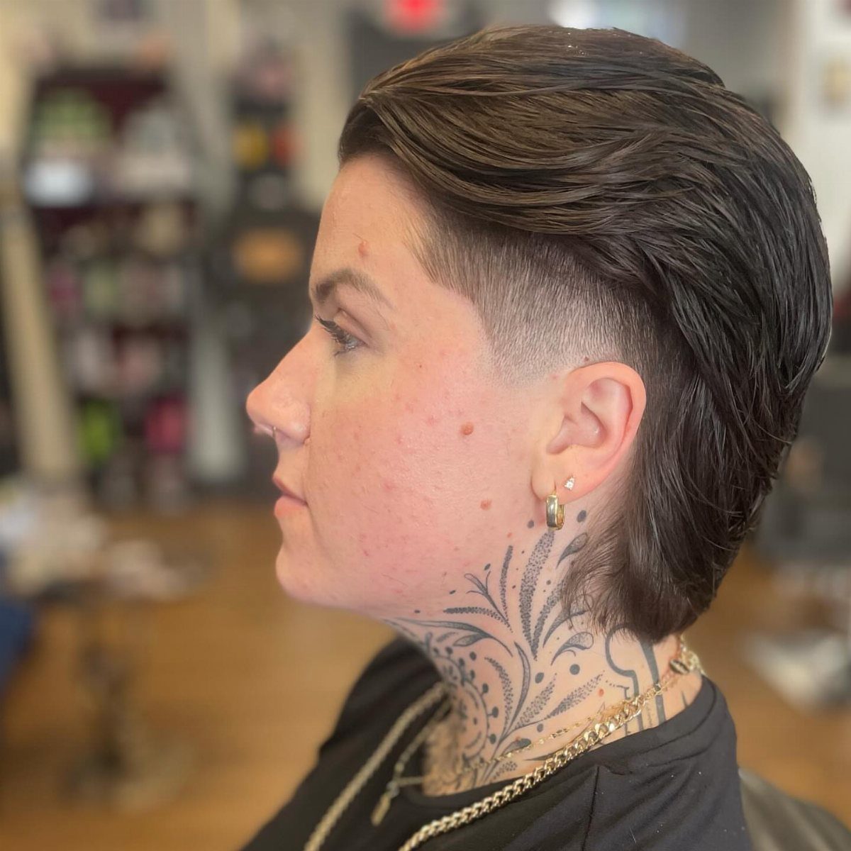 Person with a slicked-back modern mullet haircut and a detailed neck tattoo.