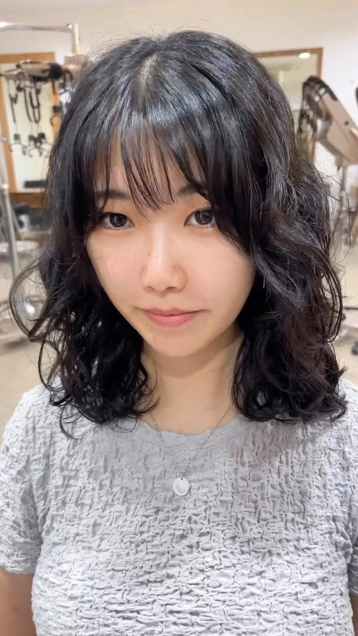 10 Natural Curls Hairstyles for Every Length and Style 5 Woman with bouncy shoulder-length black curls and bangs in a salon setting.