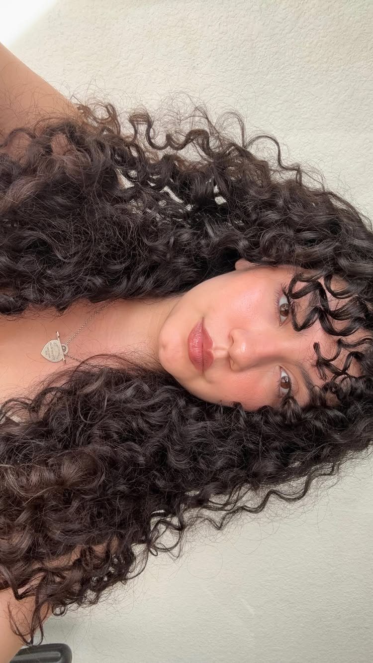 10 Natural Curls Hairstyles for Every Length and Style 9 Person with voluminous dark brown curly hair and textured curly bangs framing their face.