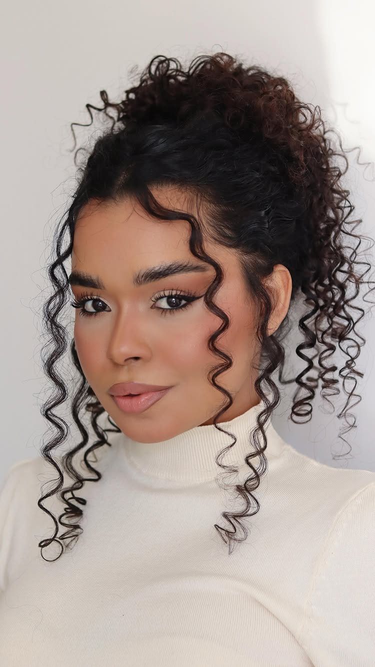 10 Natural Curls Hairstyles for Every Length and Style 1 Woman with dark curly hair in a high bun and face-framing spiral curls.