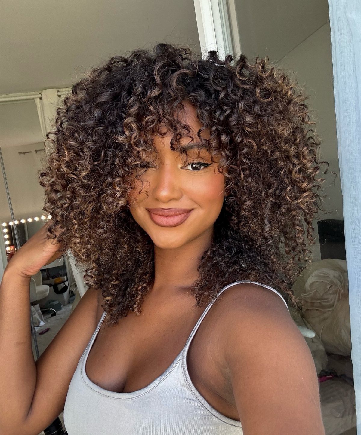 10 Natural Curls Hairstyles for Every Length and Style 2 Woman with voluminous brown curly hair and face-framing layers smiling for a portrait.