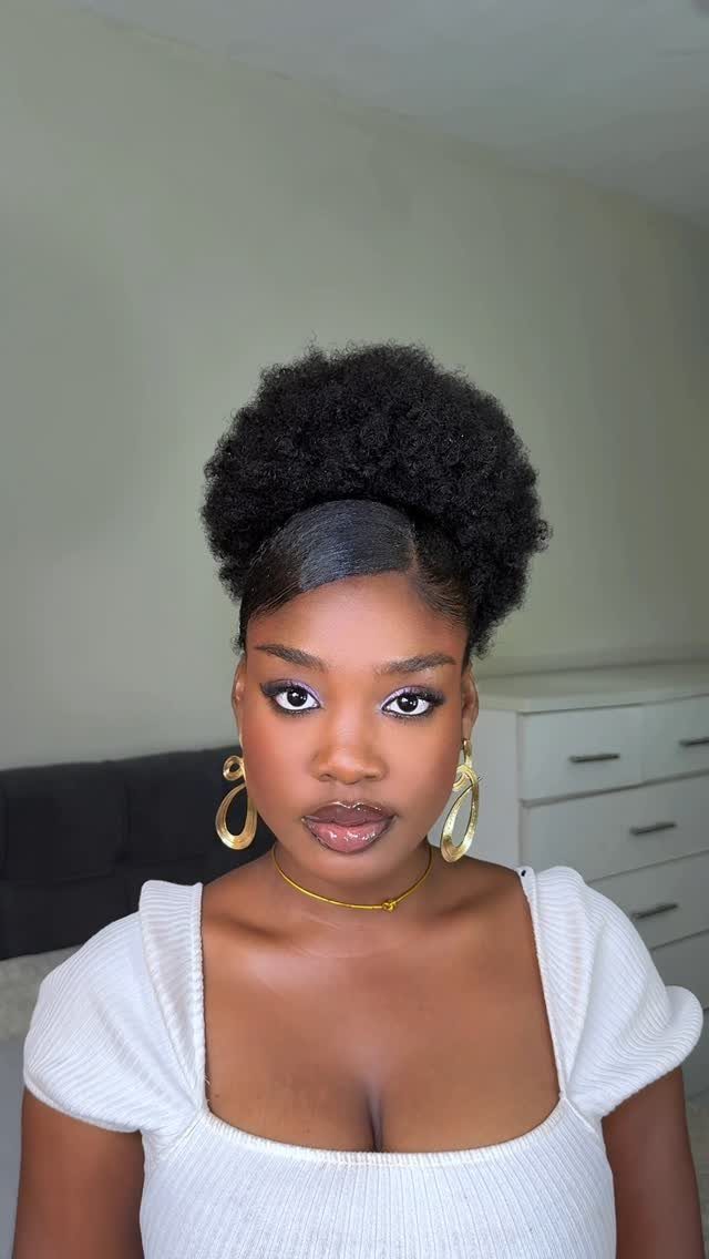 Natural Hair Beauty Looks: 11 Styles From Buns to Locs 9 Woman with a voluminous afro hairstyle wearing gold jewelry and a white top.