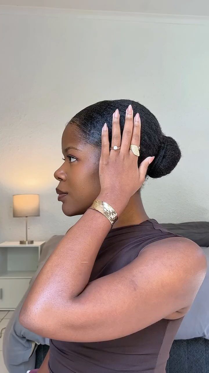 Natural Hair Beauty Looks: 11 Styles From Buns to Locs 1 Woman with dark hair styled in a sleek low bun wearing gold jewelry.