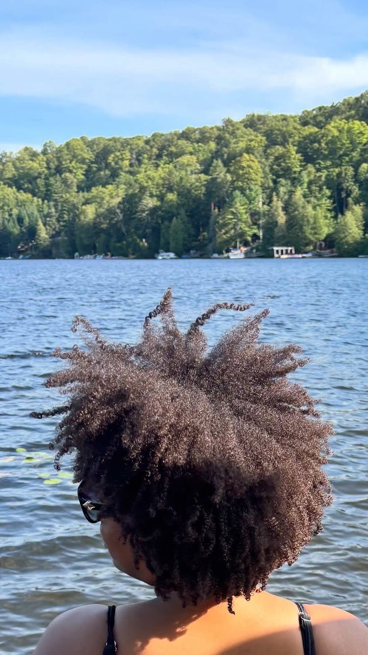 Natural Hair Beauty Looks: 11 Styles From Buns to Locs 7 Natural curly hair in a voluminous style overlooking a lake and green hills.