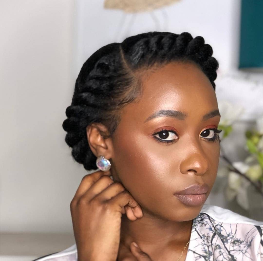 Woman with a braided updo hairstyle and glowing makeup posing for a portrait.