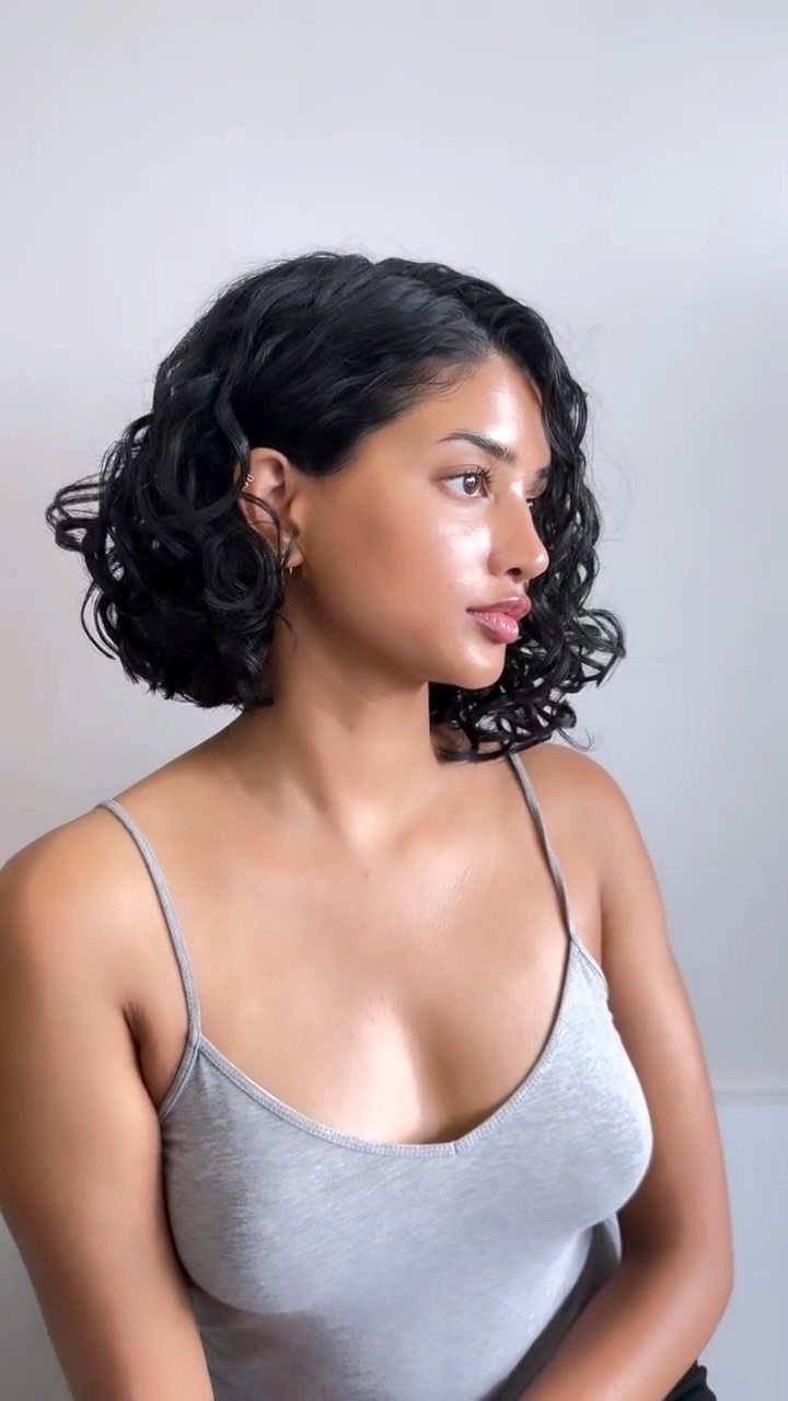 Woman with a short curly black bob hairstyle wearing a grey top.