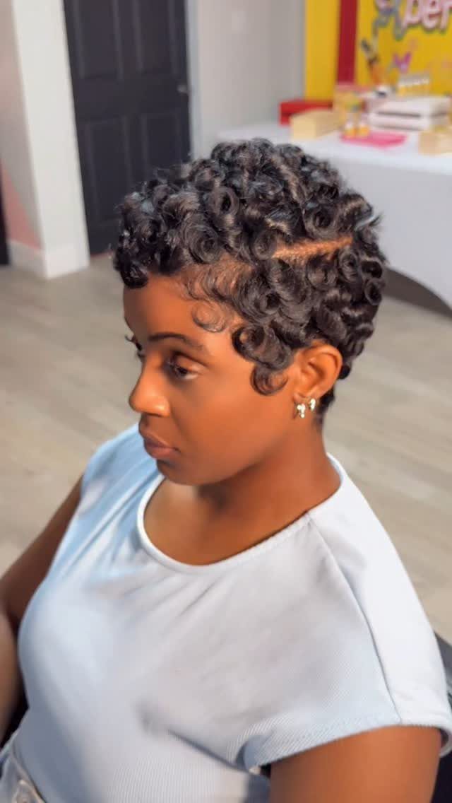 Woman with a short curly pixie cut wearing a light blue t-shirt.