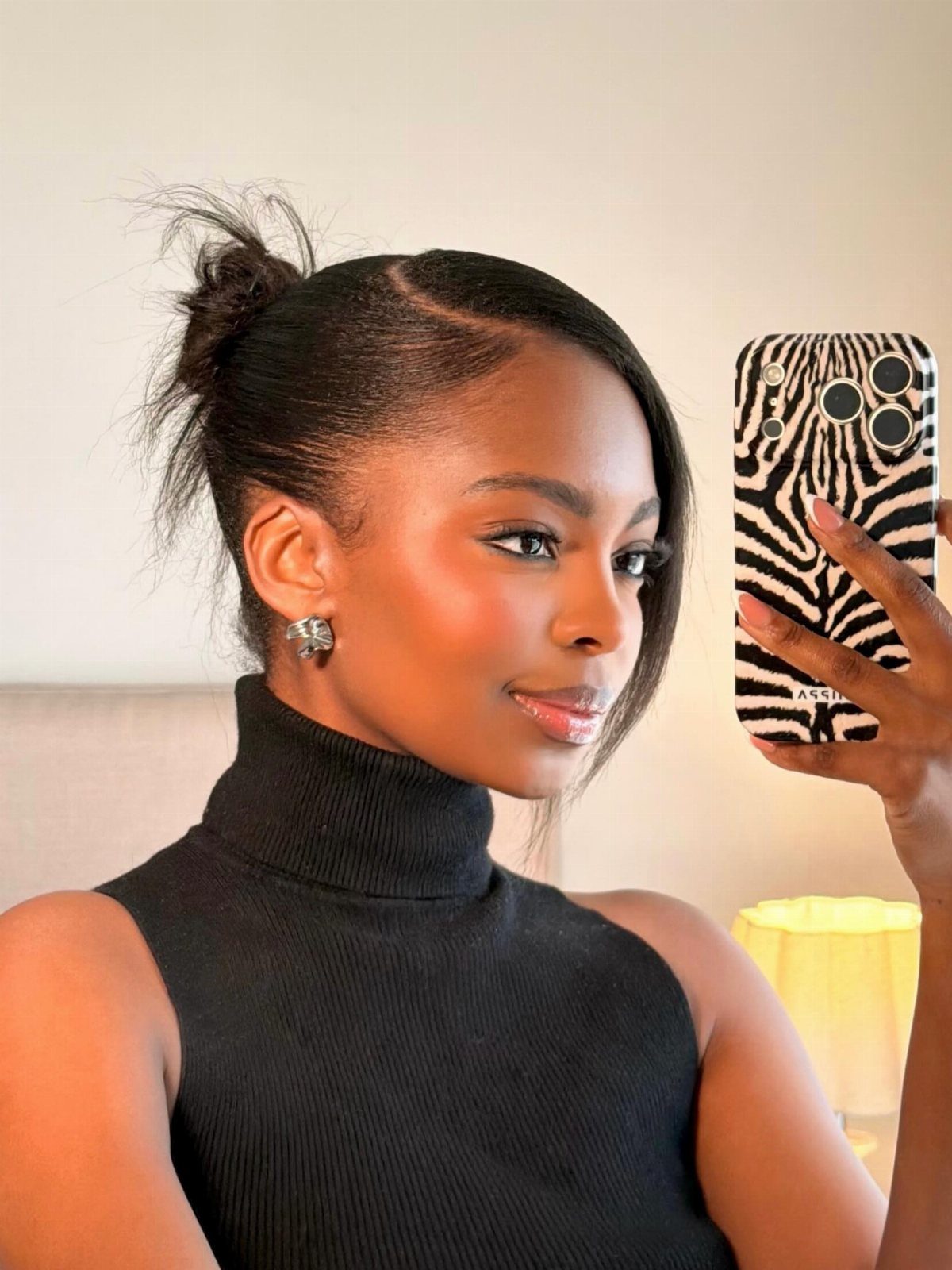 Woman with a polished slick back hairstyle and a small bun in a selfie.