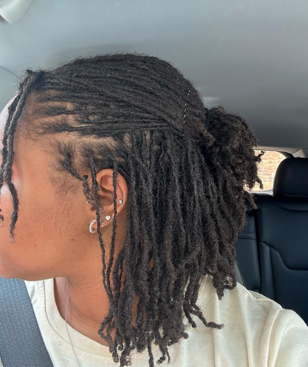Person with dark brown starter locs tied back in a low ponytail.