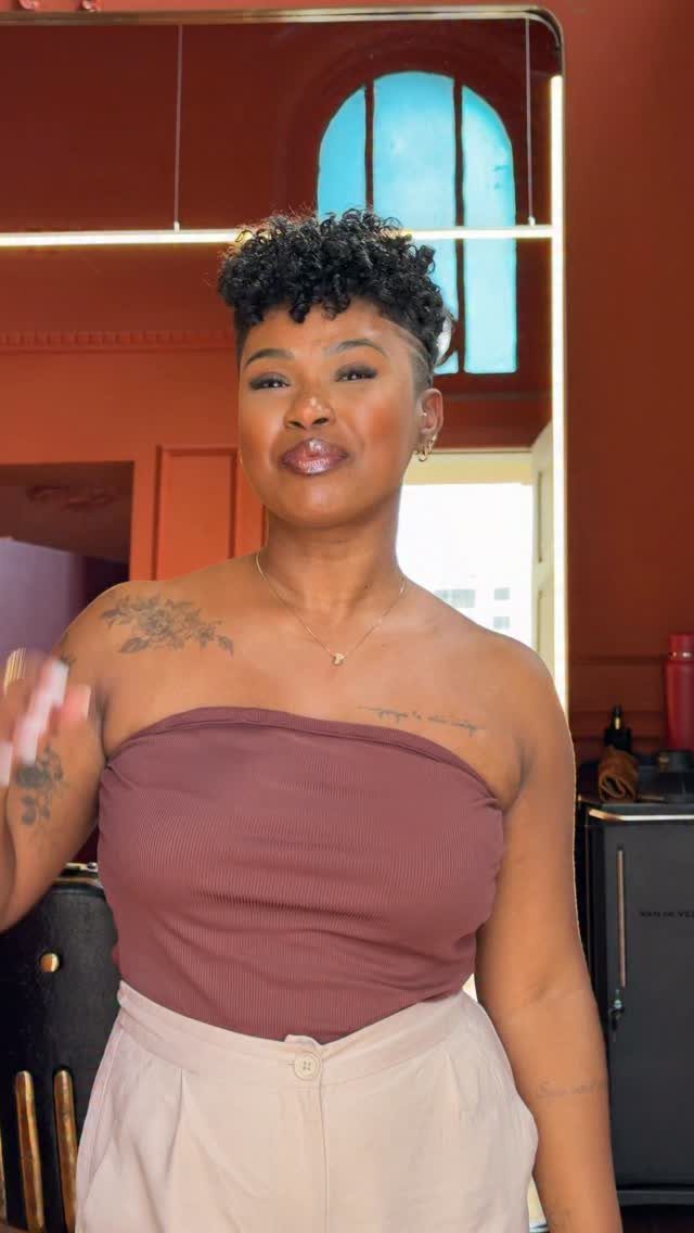 Woman with a tapered natural haircut and curly top posing in a room.