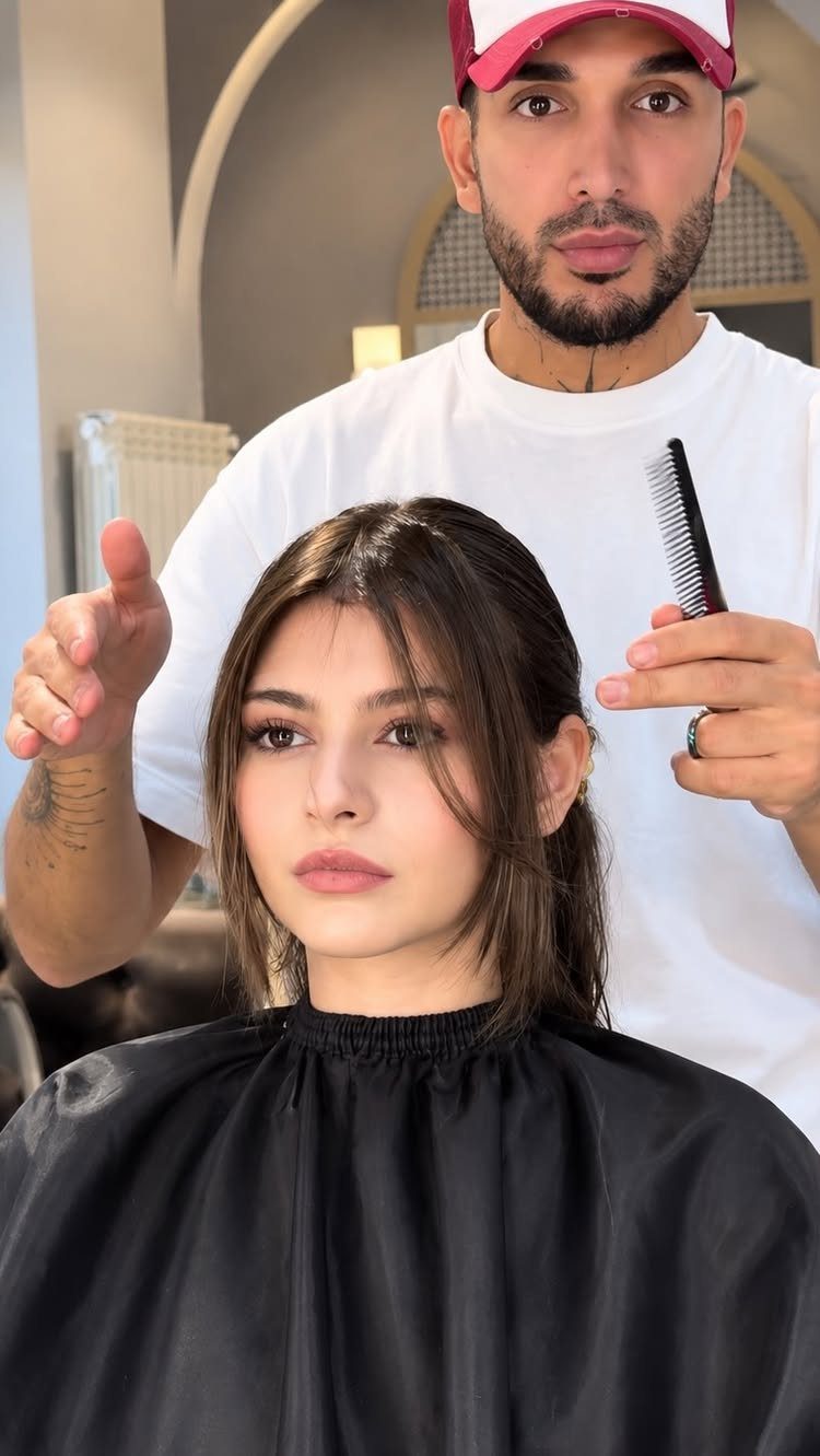 Woman with brown face-framing layers and a hairstylist standing behind her in salon.