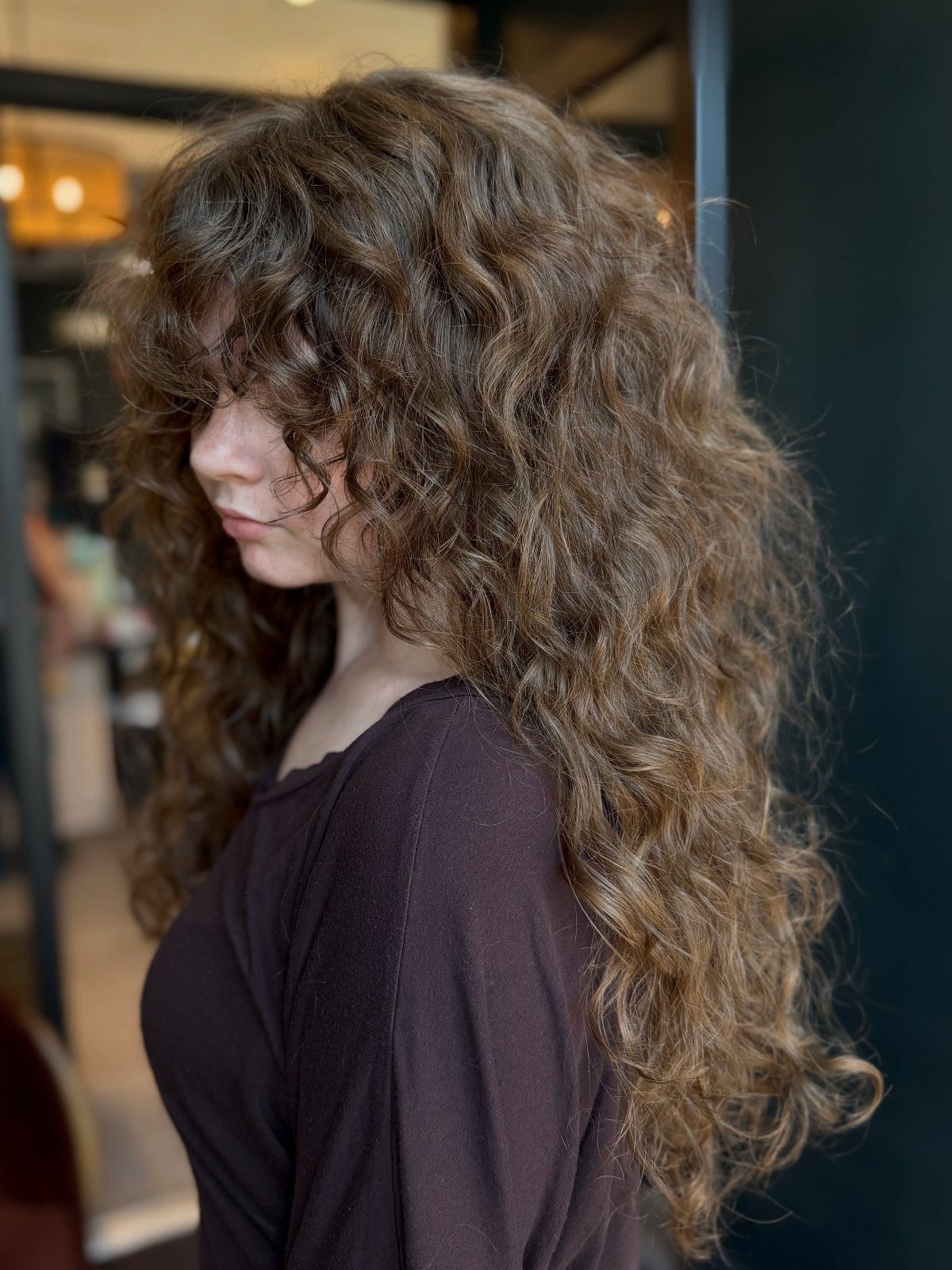 Woman with long, curly brown hair in a heavily layered shag cut with bangs.