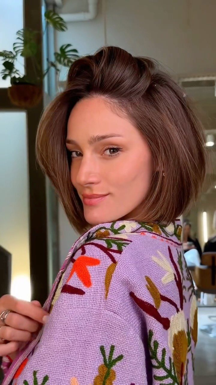 Woman with a voluminous brown soft Italian bob and purple floral jacket.