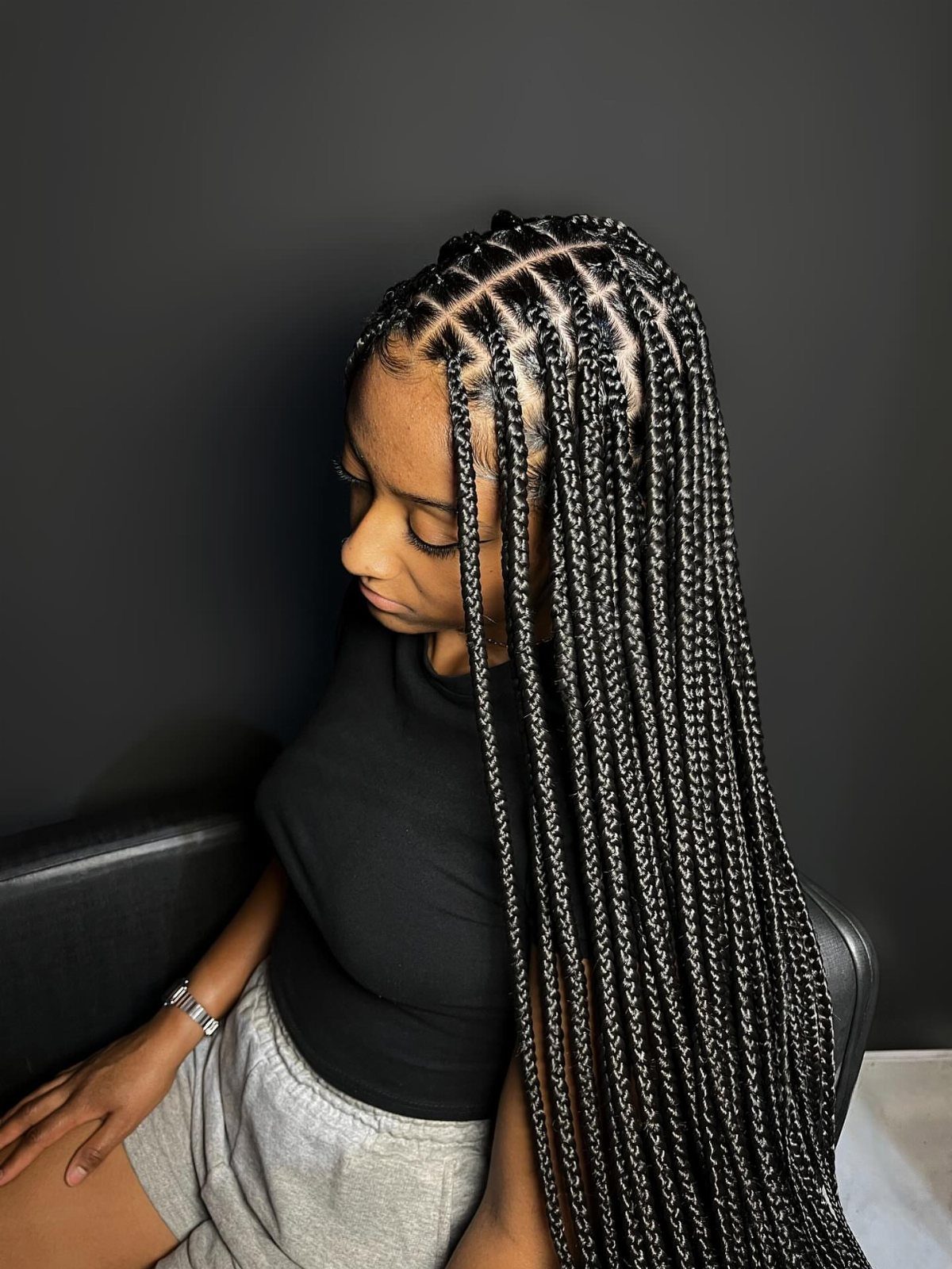Woman with long black box braids wearing a black t-shirt and grey shorts.