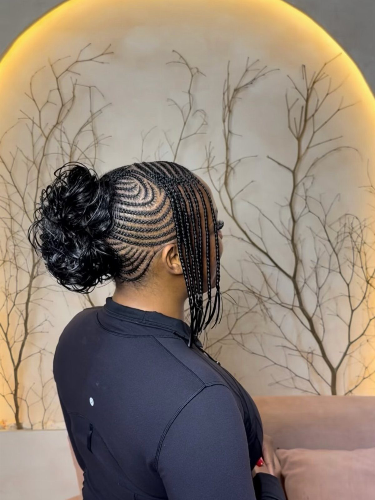 Woman with curved cornrows leading into a curly bun and hanging braids.