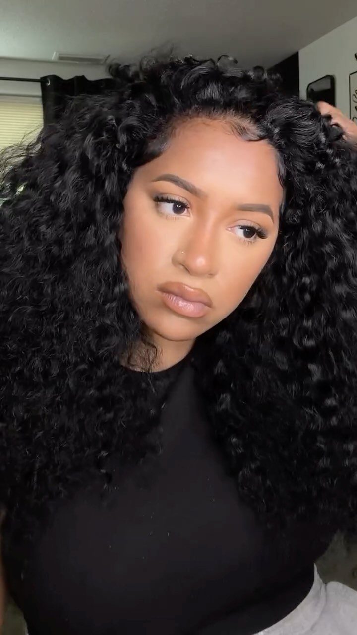 Woman with long, voluminous curly black hair wearing a simple black top.