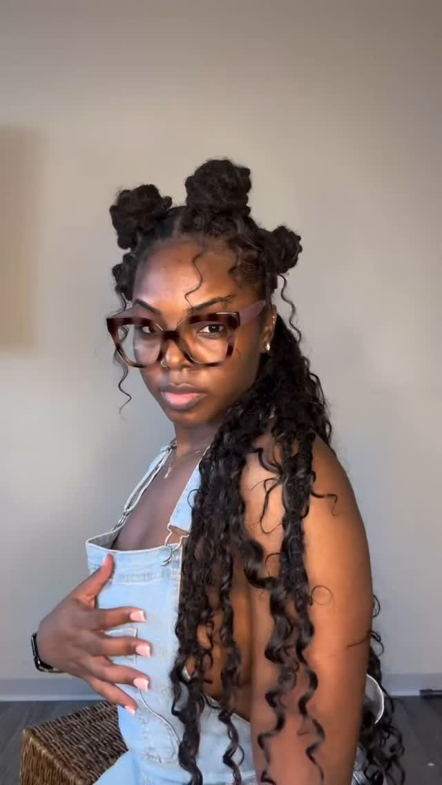 Woman with long curly faux locs and three small buns on top.