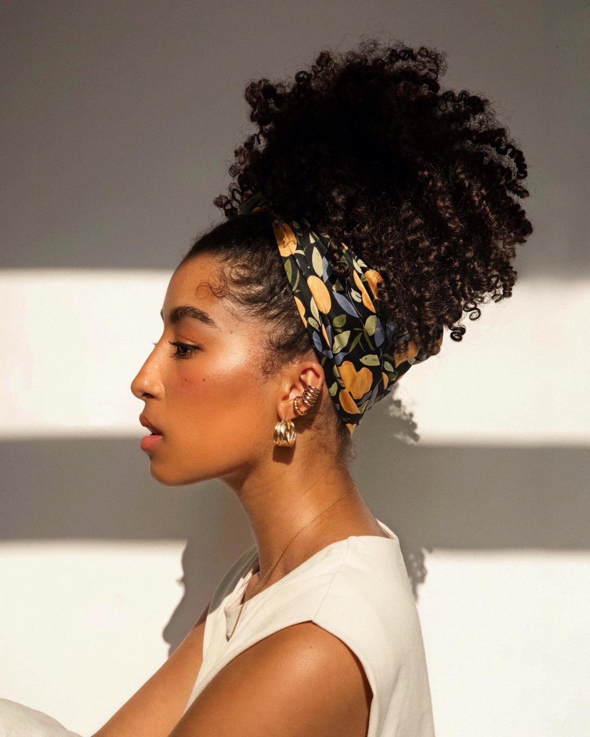 Woman with curly hair in a high pineapple updo wrapped in a floral scarf.