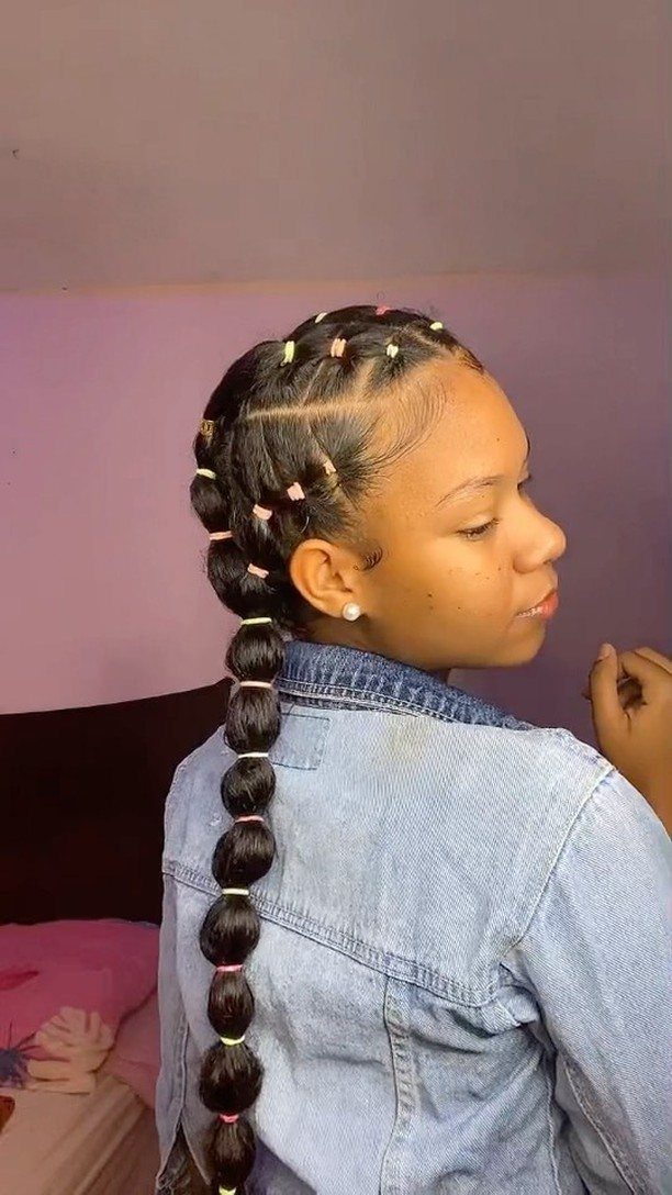 Woman with a bubble ponytail secured by colorful rubber bands wearing a denim jacket.